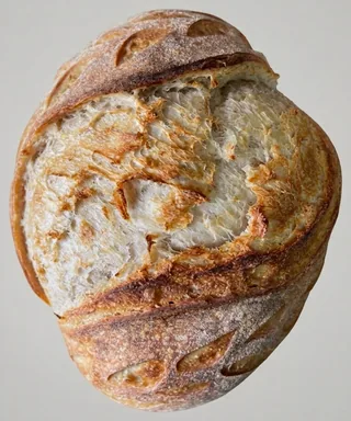 A round artisan sourdough loaf with a deeply scored, golden-brown crust dusted with flour.